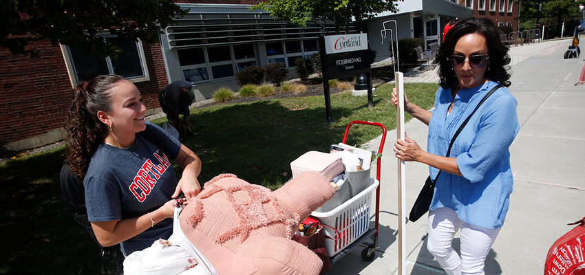 A woman carrying a mirror and helping her daughter move in to her residence hall