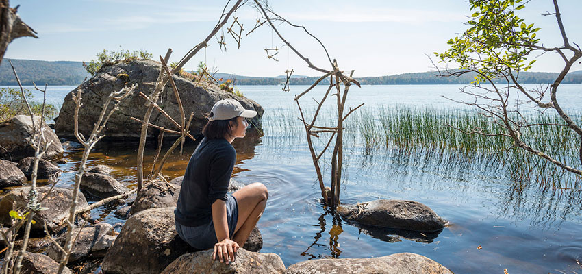 Student sitting along the shore of Raquette Lake