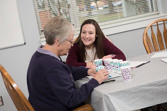 A graduate student sitting at a table with an elderly woman with cups in front of them