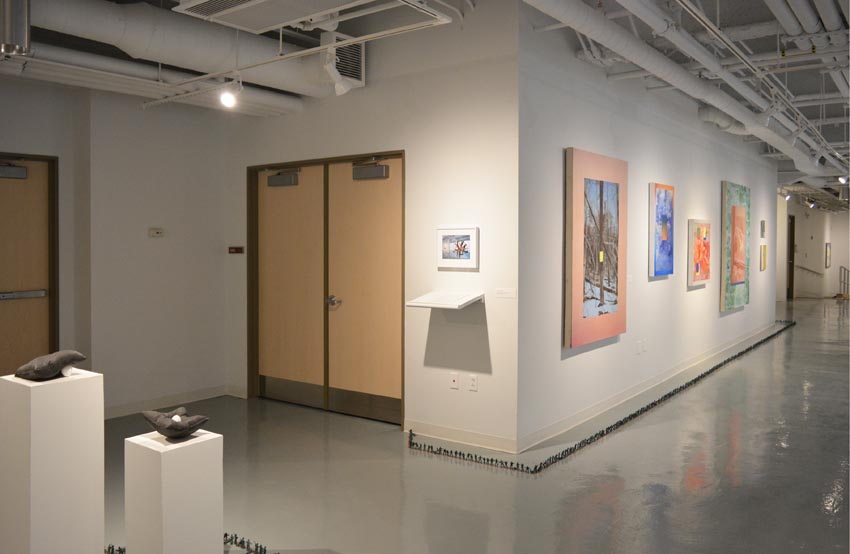 View into the central gallery at Dowd Gallery featuring sculptural objects produced by Jaroslava Prihodova, director of the Dowd Gallery, Wylie Schwartz, professor of art history, paintings by Stephen Alexander Clark, processor of painting, and floor installation by Bryan Valentine Thomas, instructor of design and drawing, at the Art and Art History Department.