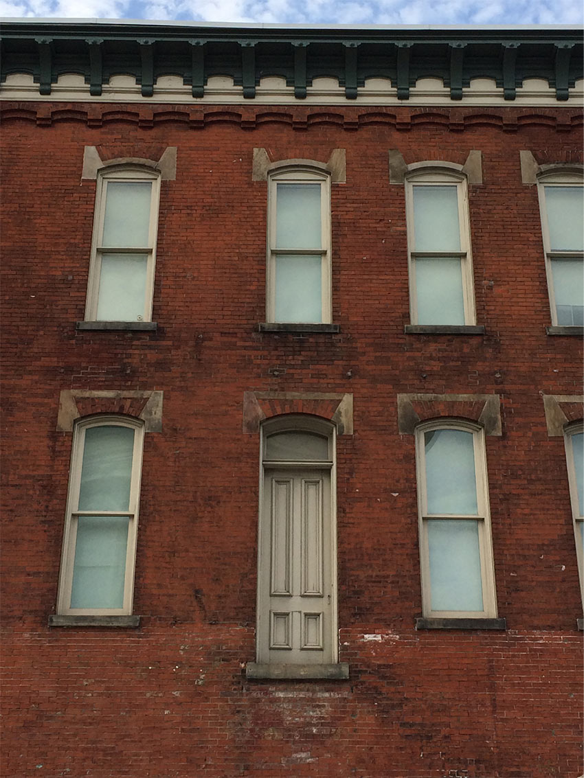 A brick building facade with windows and an inaccessible door above ground level